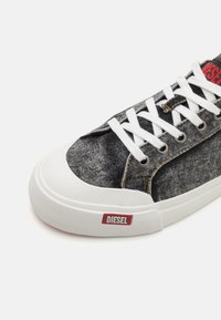 Denim sneaker with a gray fabric upper, white rubber sole, and red "DIESEL" logo. Features white laces and metal eyelets for added detail.