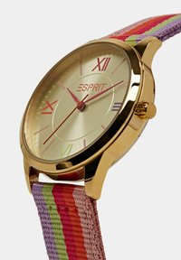 Goldfarbene Uhr mit einem cremefarbenen Ziffernblatt, bunten Stundenmarkierungen und einem gestreiften Textilarmband in Pink-, Grün- und lila Tönen.