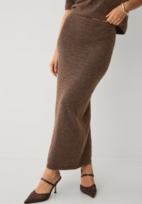 Lange bruine gebreide rok gemaakt van zacht materiaal, met een slim fit en een hoge tailleband. Gecombineerd met bruine sandalen met bandjes.