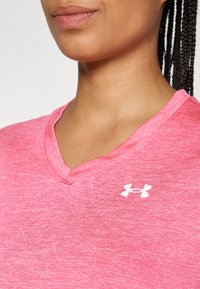 Roza majica z v-izrezom, izdelana iz mehkega teksturiranega materiala. Ima belo logo Under Armour na prsih.