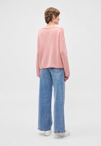 Camisola rosa de malha larga com decote largo e ombros caídos, combinada com jeans de perna larga azul claro e sapatilhas brancas.