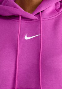 Sudadera fucsia hecha de tela suave, con un logo de Nike blanco, cordones y un bolsillo tipo canguro. Textura lisa con detalles de costura.