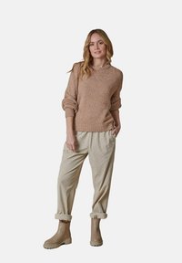 Strickpullover in Hellbraun mit umgeschlagenen Bündchen, kombiniert mit beigen, strukturierten Hosen und kastanienbraunen Stiefeletten, alles in einem lässigen Schnitt.