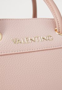 Pink textured leather handbag featuring gold "VALENTINO" logo, decorative stitching, and circular gold hardware accents.