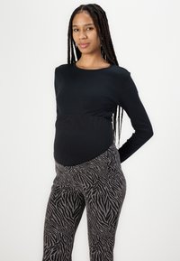 Svart ribbet langermet topp kombinert med grå og svart zebra-mønstret bukse. Toppen har en tettsittende, elastisk design som tilpasser seg en mage.