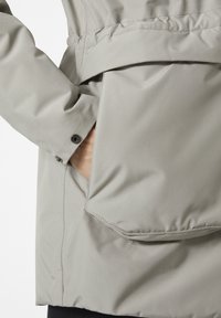 Light gray waterproof jacket featuring a pocket with a flap, elastic waist, and buttoned cuff detail. Smooth texture and minimalist design.