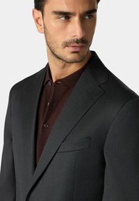 Giacca di suit grigio scuro su misura con revers a punta, abbinata a una camicia color bordeaux con colletto, dotata di due bottoni e una texture liscia.