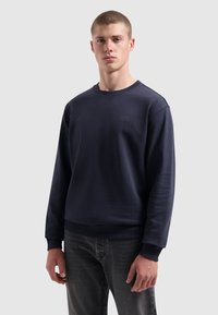 Donkerblauwe sweatshirt van zacht materiaal met rib gebreide mouwen en onderrand. Kenmerkt zich door het minimalistische "PURE PATH" logo op de borst. Klassiek ontwerp met ronde hals.