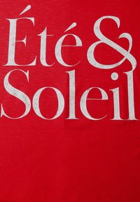 Tela roja con texto grande y blanco con textura que dice "Été & Soleil" en una fuente serif negrita y elegante.