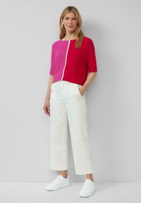 Korte mouwen top in levendig roze en magenta, met een witte naad aan de voorkant; gecombineerd met witte wijde broek en witte sneakers.