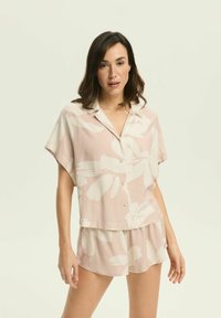 Jasnoróżowa bluzka z krótkim rękawem w białe kwiatowe wzory, zapinana na guziki, w komplecie z pasującymi szortami, oba wykonane z miękkiego materiału.