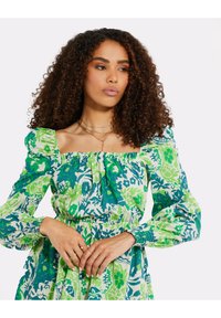 Abito stampato floreale in blu e verde, con scollatura quadrata, maniche a sbuffo, vita arricciata e tessuto raccolto per una texture unica.