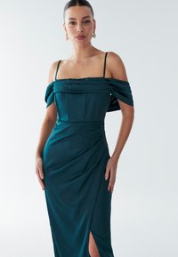 Teal satijnen avondjurk met off-the-shoulder mouwen, aansluitend lijfje en een gedrapeerde rok met een hoge split tot boven de dijen.