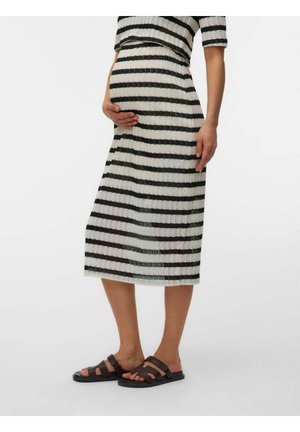 Personne enceinte portant une robe rayée noir et blanc et des sandales noires, tenant doucement son ventre d’une main.