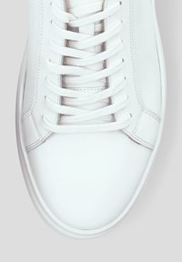 Białe skórzane sneakersy o gładkiej fakturze, z płaskimi białymi sznurówkami i minimalistycznym przeszyciem po bokach. Zaokrąglony nosek i prosty design.