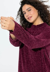 Maglione borgogna in peluche con maniche lunghe, collo alto e polsini a costine. Presenta una texture morbida e una silhouette rilassata.
