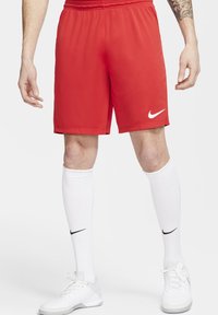 Pantalones cortos deportivos rojos de Nike con una cinturilla elástica y un logo blanco de Nike. Llevados con calcetas blancas hasta la rodilla y zapatillas deportivas blancas.