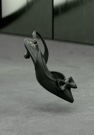 Chaussure à bride arrière en cuir noir avec bout pointu et nœud décoratif, dotée d'un petit talon et d'une boucle dorée. Surface plate en dessous.