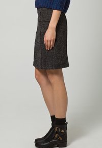 Falda hasta la rodilla de mezcla de lana en gris oscuro con textura sutil, que presenta una silueta estructurada y bolsillos traseros. Combinada con botines negros hasta el tobillo.