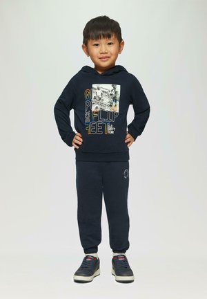 Marineblauwe hoodie met grafische print en tekst, gecombineerd met bijpassende sweatpants. Voorzien van elastische manchetten en casual sneakers.