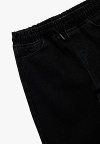Czarne dżinsowe joggery z elastycznym pasem i sznurkiem do regulacji. Posiadają boczne kieszenie oraz teksturowany materiał z delikatnym połyskiem.