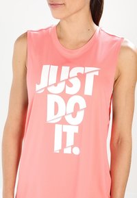 Top atletico senza maniche di colore rosa con una texture liscia, caratterizzato da un audace testo bianco "JUST DO IT." Il design stampato copre la parte anteriore.