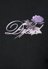 Μαύρο ύφασμα με καλλιγραφικό κείμενο 'Diesel', επικάλυψη από μωβ τριαντάφυλλο με φύλλα και μίσχο που εκτείνονται κατά μήκος της λέξης.