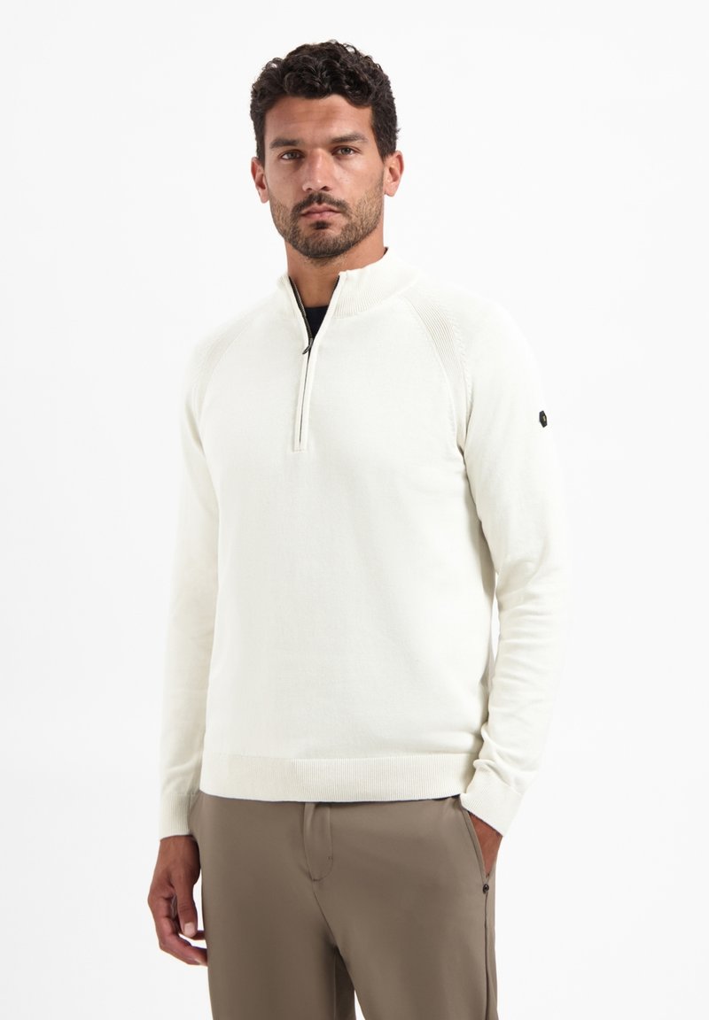Crème-kleurige pullover met een halve rits en ribbelaccenten op de schouders, en een getailleerde zoom. Combineer met beige broek voor een samenhangende look.
