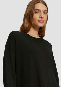 Zwarte oversized trui van zachte stof, met een ronde hals en verlaagde schouders. Eenvoudig ontwerp zonder zichtbare patronen of accenten.