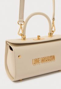 Τσάντα χειρός από μπεζ τεχνητό δέρμα με μεταλλικά χρυσά στοιχεία, δομημένο σχήμα, επάνω λαβή και ανάγλυφο λογότυπο "LOVE MOSCHINO" στο μπροστινό μέρος.