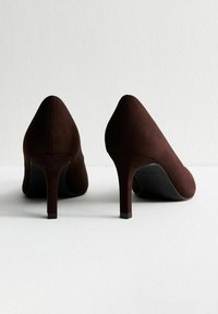 Scarpe con tacco alto in suede marrone con punta affusolata e design elegante. Presentano un tacco a stiletto sottile e una texture liscia e opaca.