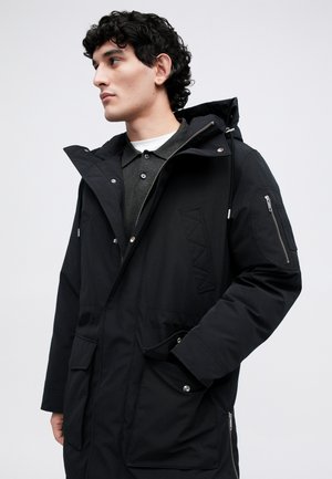 Parka preta com fecho zip, capuz ajustável, múltiplos bolsos, acabamentos texturizados e um acabamento em tecido suave.