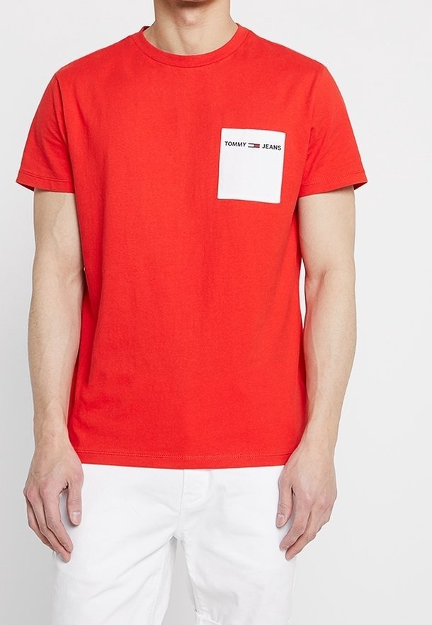 Červené bavlněné tričko s kulatým výstřihem, krátkými rukávy a bílou náprsní kapsou s černým nápisem "TOMMY JEANS". Hladký materiál, volný střih.