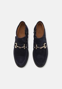 Zapatos de ante azul marino con acentos de hardware dorado, con una correa ancha en la parte superior y una cremallera lateral para un fácil acceso.