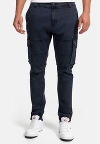 Tummansiniset cargo-housut, jotka on valmistettu kestävästä kankaasta. Housuissa on useita taskuja, kapenevat lahkeet ja joustavat resorit nilkoissa.