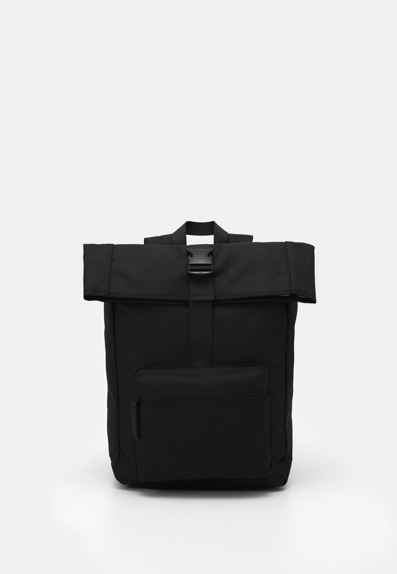 Sac à dos noir à fermeture roulante avec poche avant zippée et fermeture à boucle centrale, debout sur un fond clair uni.