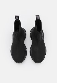Bottines noires à enfiler avec une tige en tricot côtelé, semelle en caoutchouc et languette de traction portant le logo 'Steve Madden' sur le côté.