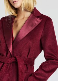 Bordeauxroter Wickelmantel mit Satin-Kragen, langen Ärmeln, strukturiertem Stoff und Gürtel zum Binden in der Taille.