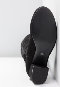 Botín de ante negro con punta redonda, parte superior texturizada y un tacón bloque bajo. Presenta un zipper lateral y una etiqueta de talla 37 en la suela.