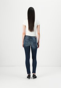 Sötétkék farmer skinny nadrág közepes derékkal, hátsó zsebekkel és enyhe kopással, hozzáillő fitted fehér pólóval és fekete magassarkúval.