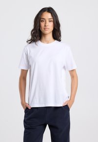 White cotton t-shirt with short sleeves, crew neck, and a relaxed fit. Smooth texture, minimal design, no visible patterns or accents.
