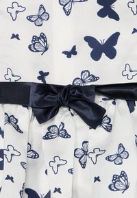 Tessuto bianco con motivo di farfalle blu scuro, dotato di una cintura in satin blu scuro con dettaglio a fiocco e sezioni della gonna plissettate.