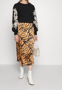 Pull noir avec broderie florale blanche sur les manches, associé à une jupe midi imprimée tigre en orange et noir, et des bottines blanches.