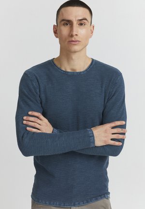 Chemise bleue à manches longues en tissu texturé, avec un col rond et des poignets contrastés. Présente un motif à carreaux subtil et une coupe régulière.