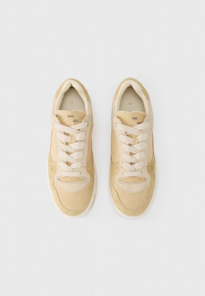 Μπεζ αθλητικά παπούτσια από ύφασμα με σουέντ λεπτομέρειες, στρογγυλεμένη μύτη, χαρακτηριστικό σχέδιο με κορδόνια και μαλακή λευκή σόλα. Καθαρό, μινιμαλιστικό στυλ.