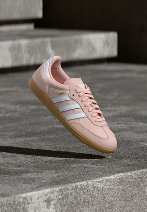 Pink leather sneaker with white leather stripes, herringbone pattern, and gum rubber sole. Features textured heel and gold logo detailing.