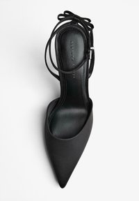 Fekete magas sarkú cipő hegyes orral, szatén felülettel és vékony bokapántokkal, amelyek hátul masniba kötődnek.