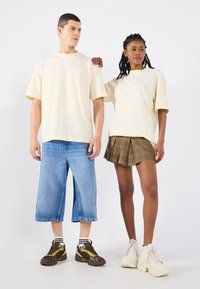 Tej színű, oversized pólók, kék, bő fazonú farmernadrág, barna kockás redőzött szoknya, fehér sportcipők és mintás zoknik.