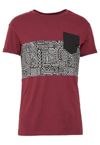 Mörkröd t-shirt med ett geometriskt svart-vitt mönster över bröstet, med en liten svart ficka på v änster sida. Mjuk tygtextur.
