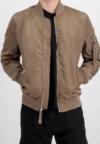 Giacca bomber marrone chiaro con zip frontale, polsini e orlo a costine, e tasche laterali. Materiale liscio e lucido con tasca con zip sulla manica.
